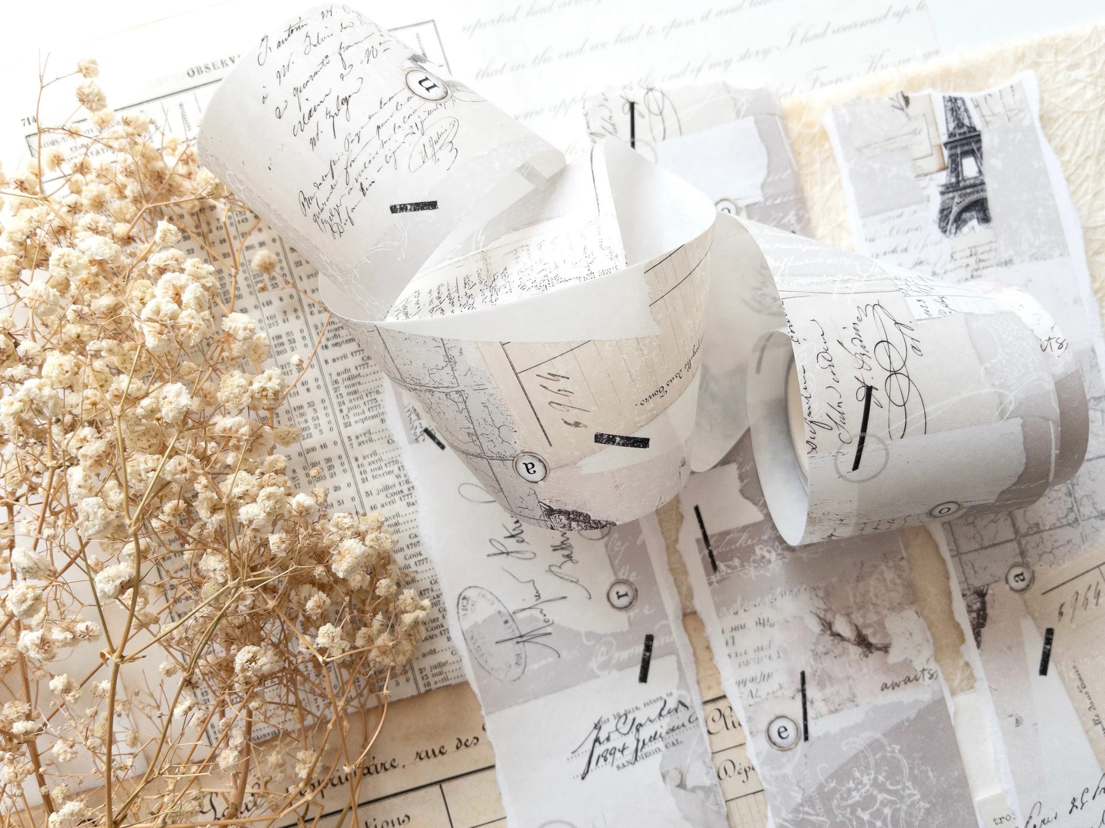 Decorative washi tape with vintage designs on a white surface with dried flowers.