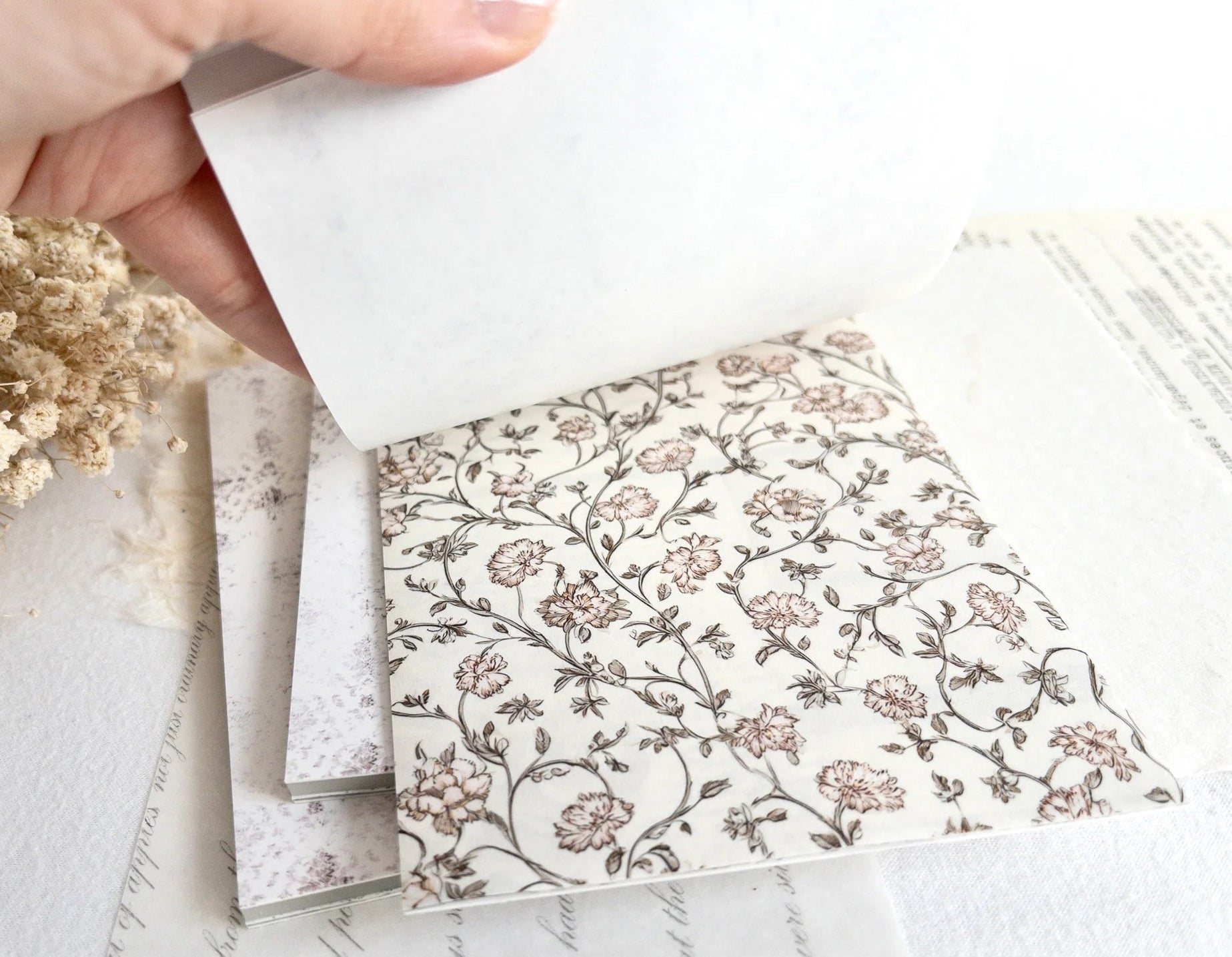 Hand flipping through sticker book with floral designs on a light background