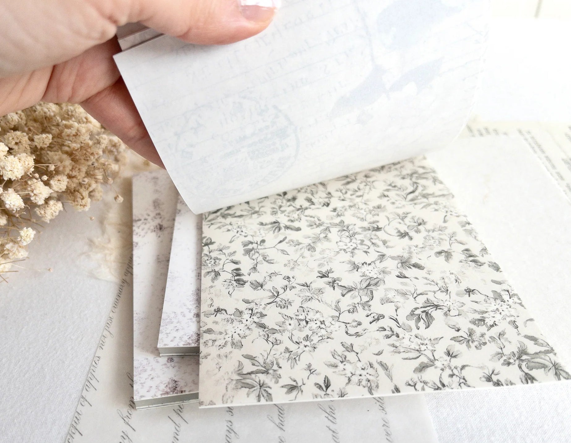 Hand flipping through sticker book with floral designs on a light background