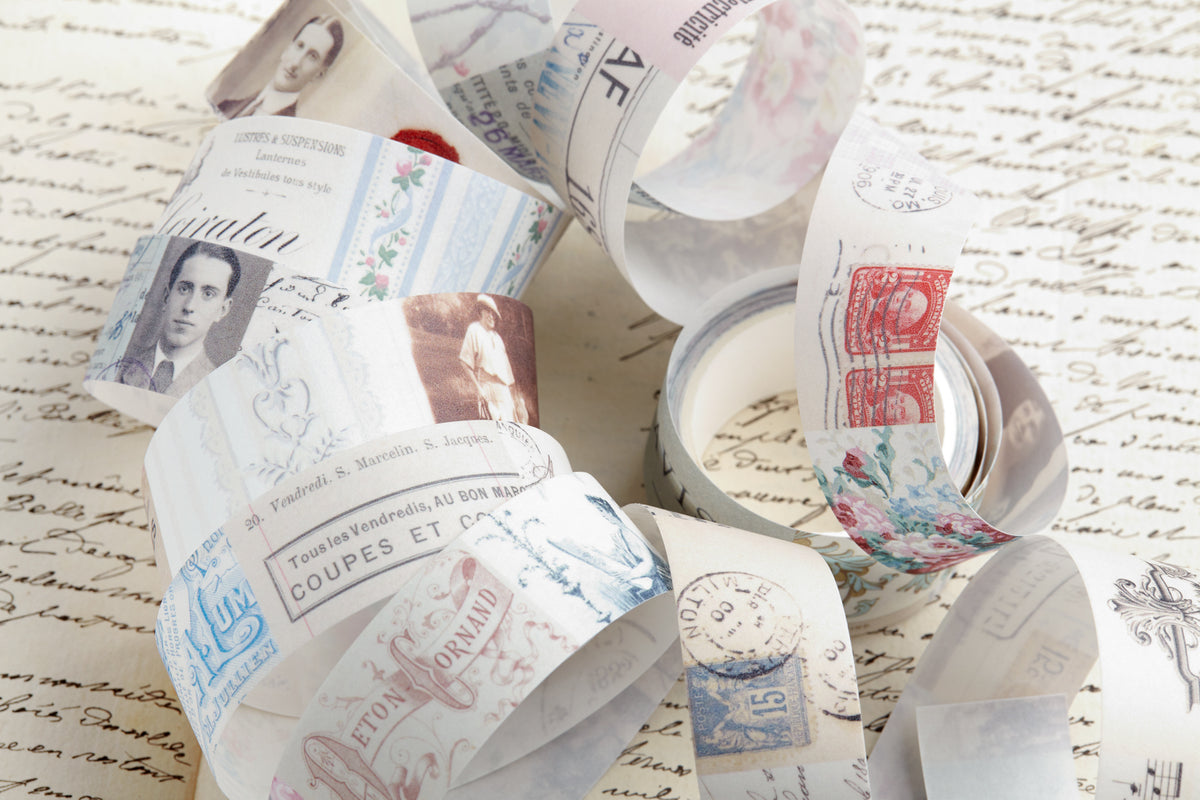 A collection of decorative washi tape printed with vintage postage stamps, postmarks, and classic portraits, arranged on top of a background of handwritten paper.
