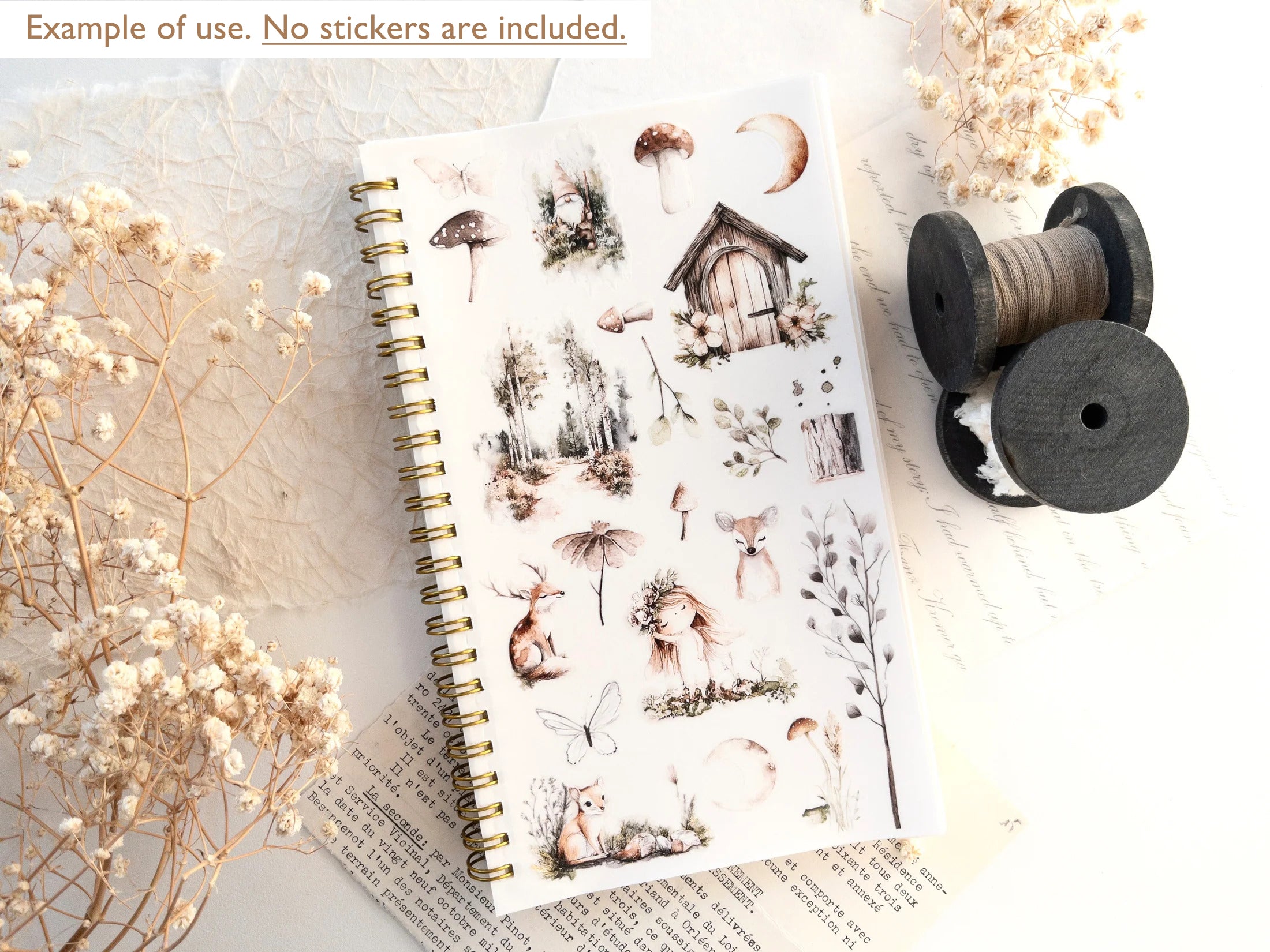 Notebook with nature-themed stickers on a textured surface with dried flowers and spools of thread.