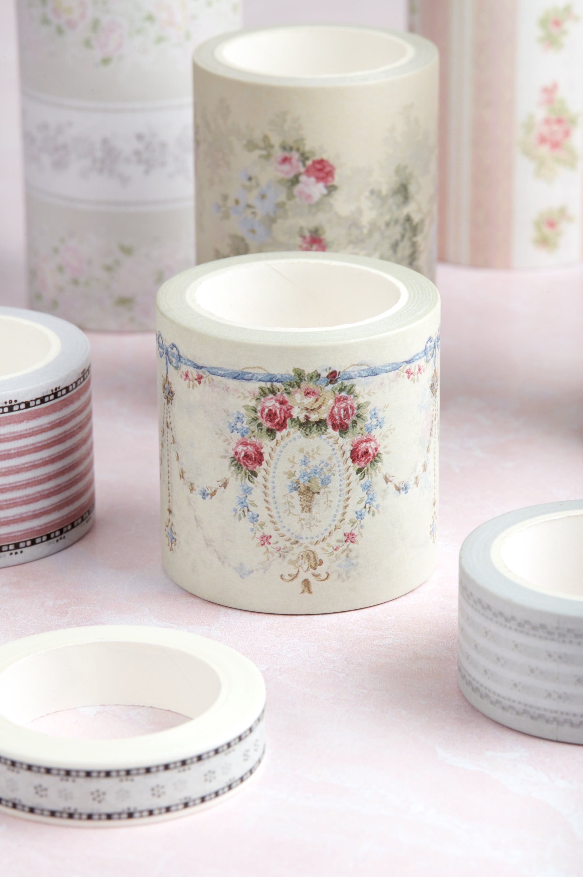 A collection of decorative washi tapes with vintage floral and striped patterns, displayed on a soft pink surface.