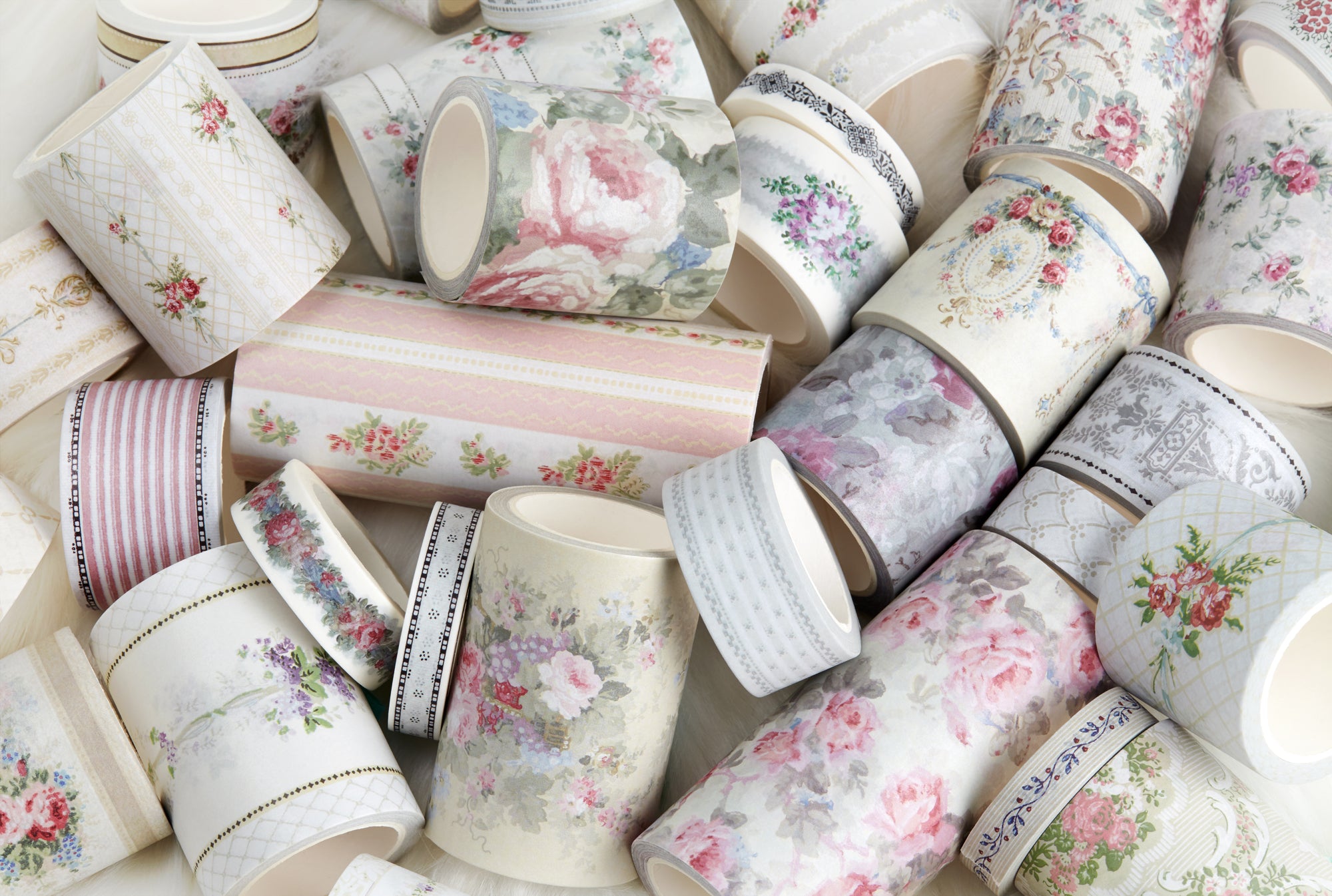 A pile of decorative washi tapes with vintage floral and patterned designs in soft pastel colors, including pink, green, gray, and cream.