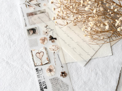 Scattered stationery stickers on PET tape, including cards, flowers, and envelopes on a textured white surface.