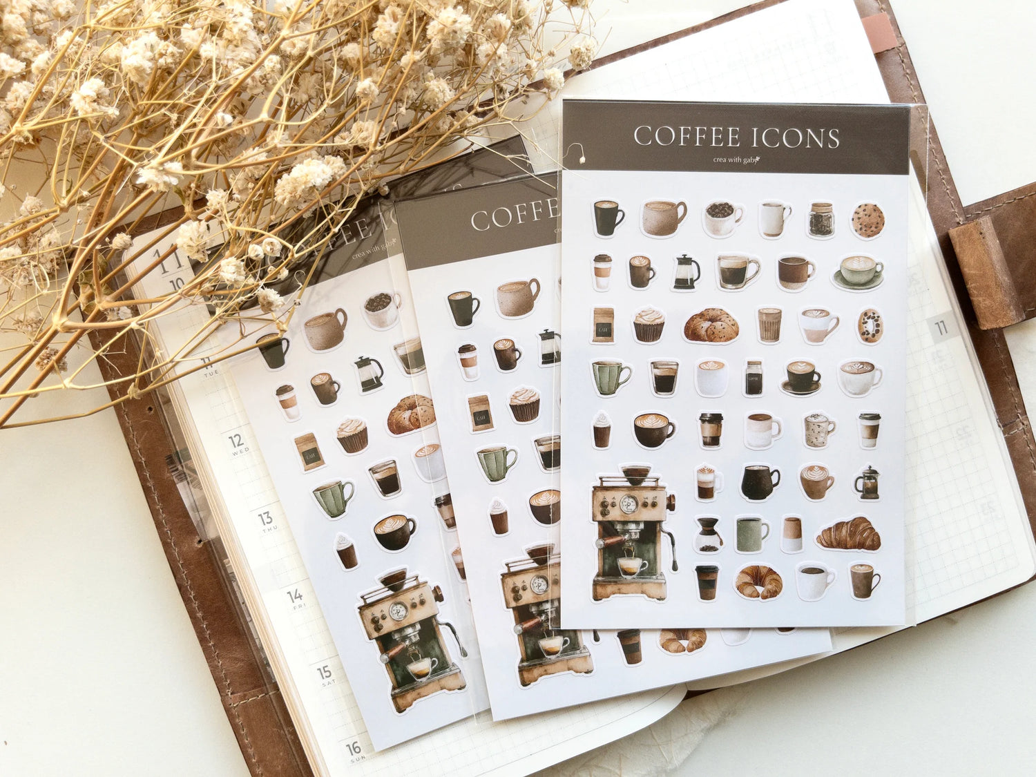 Sheets of coffee-themed mini stickers on a light surface with dried flowers.