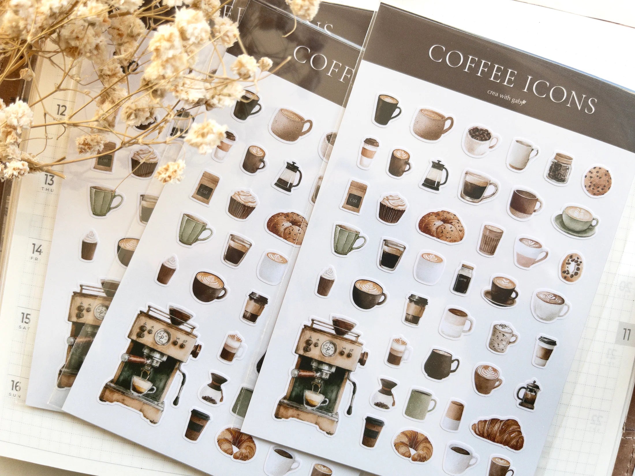 Sheets of coffee-themed mini stickers on a light surface with dried flowers.