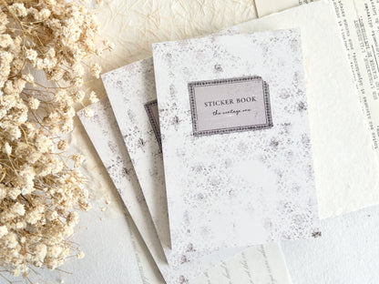 Sticker book with decorative cover on a light surface with dried flowers.