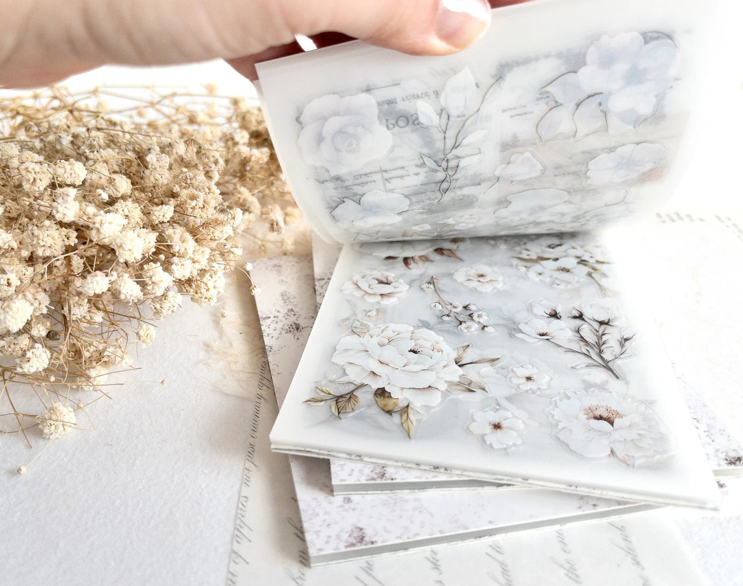 Hand flipping through sticker book with floral designs on a light background
