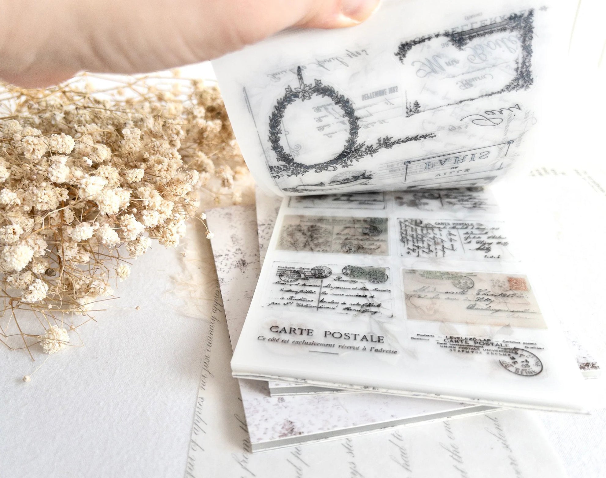 Hand flipping through sticker book with vintage-style designs on a light background