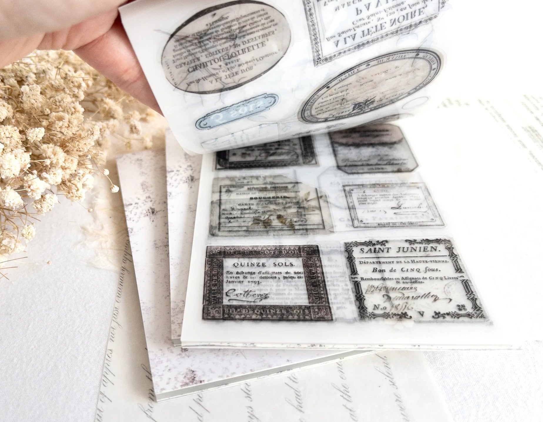 Hand flipping through sticker book with vintage-style designs on a light background