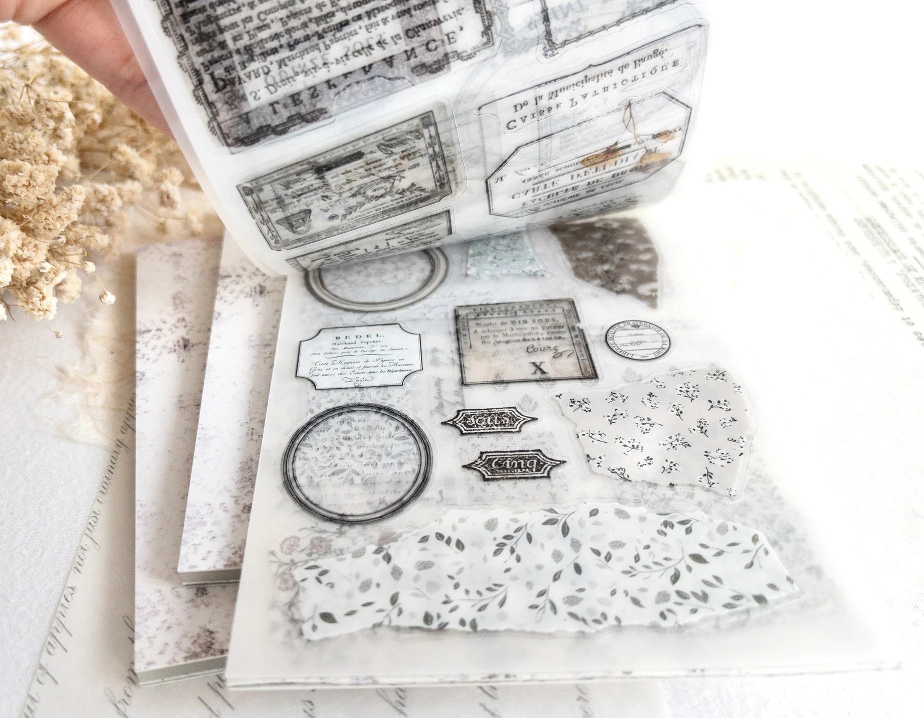 Hand flipping through sticker book with floral designs on a light background