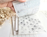 Hand flipping through sticker book with floral designs on a light background