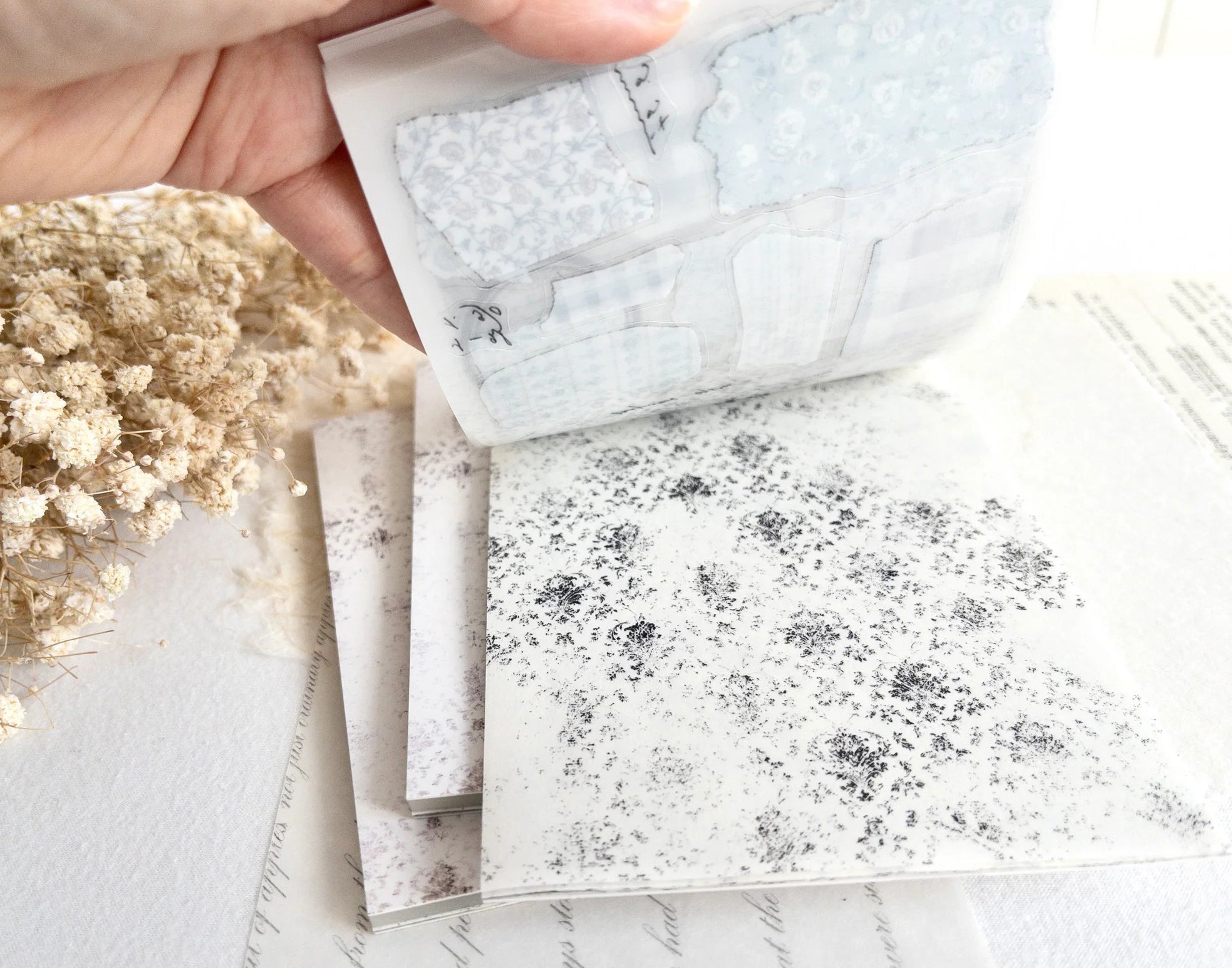 Hand flipping through sticker book with floral designs on a light background