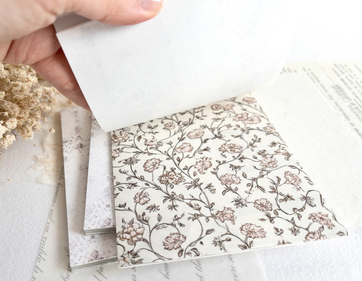 Hand flipping through sticker book with floral designs on a light background