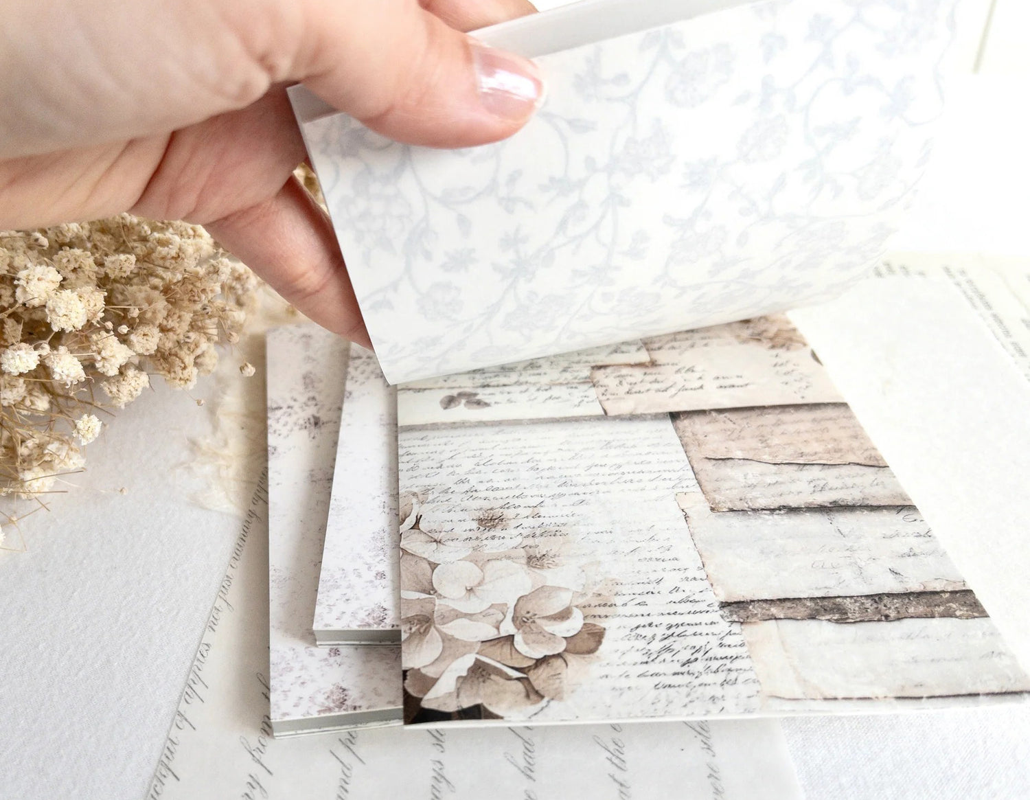 Hand flipping through sticker book with floral designs on a light background