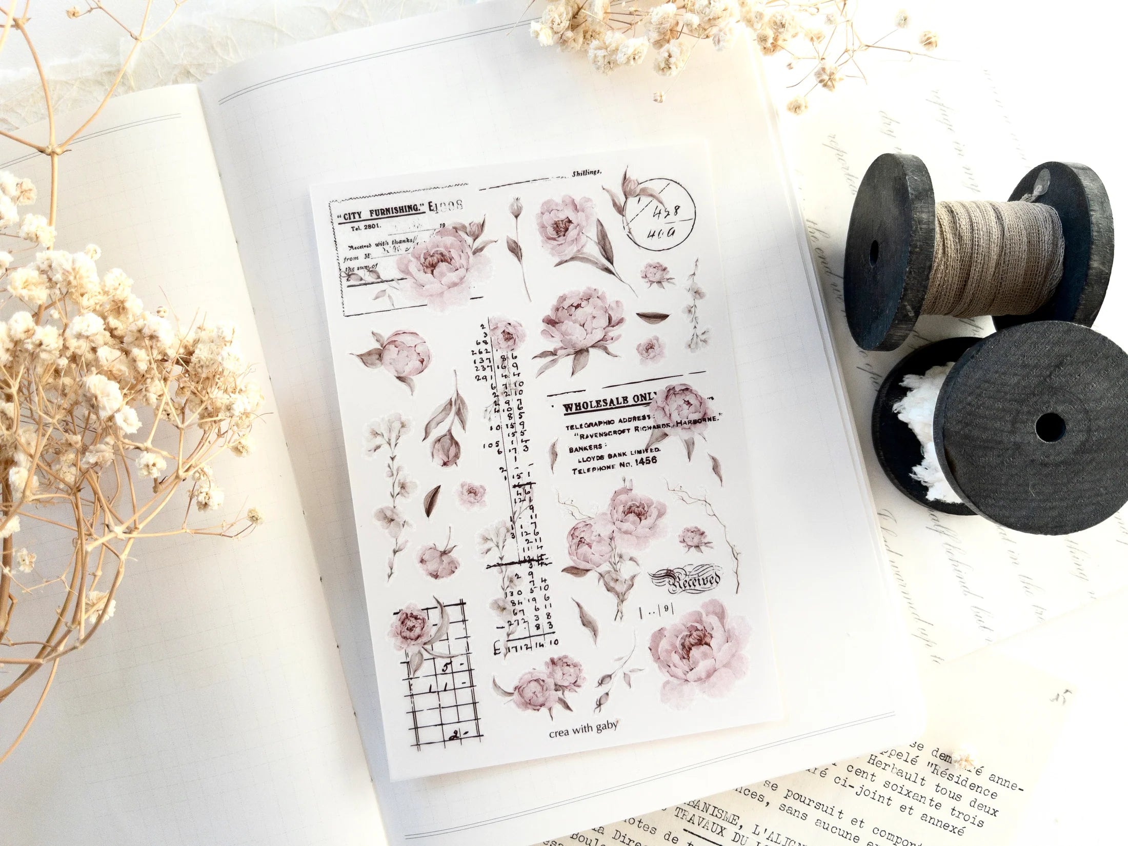 Sheet of floral and script rub-on stickers on a white surface with dried flowers and spools of thread.