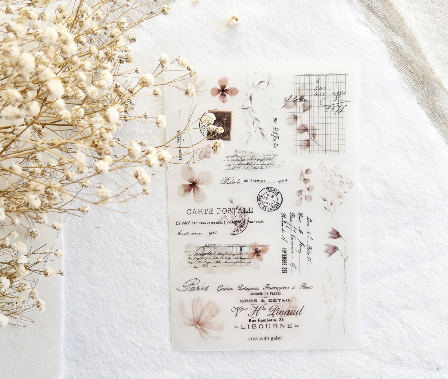 Vintage-style rub-on sticker sheet with floral designs on a textured surface with dried flowers.