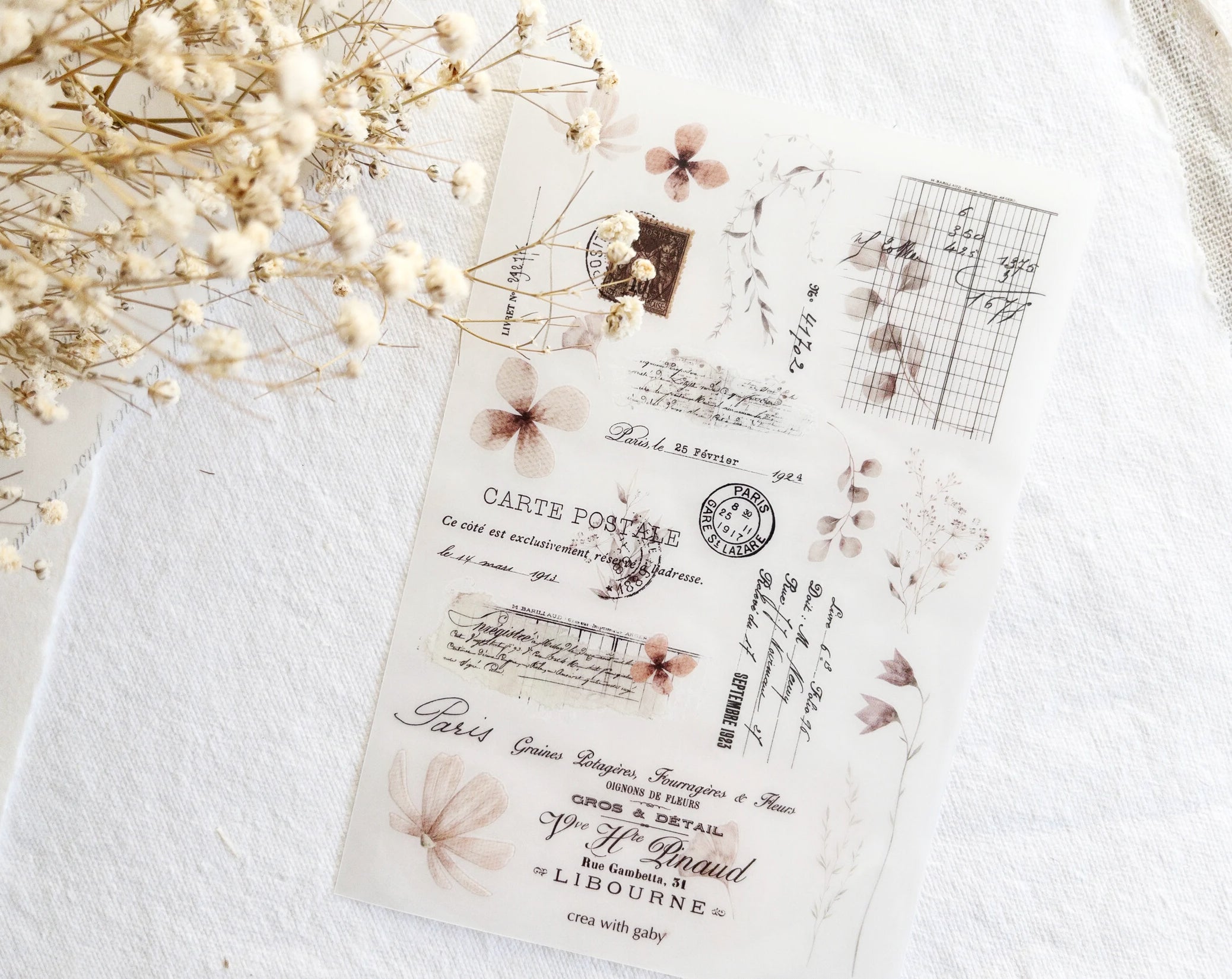 Vintage-style rub-on sticker sheet with floral designs on a textured surface with dried flowers.
