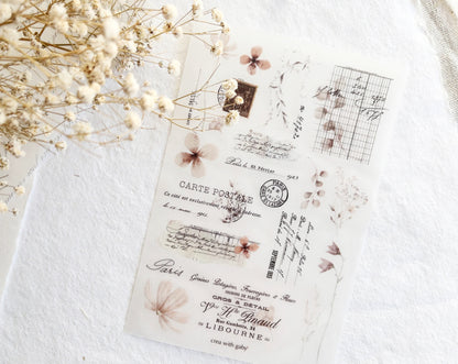 Vintage-style rub-on sticker sheet with floral designs on a textured surface with dried flowers.
