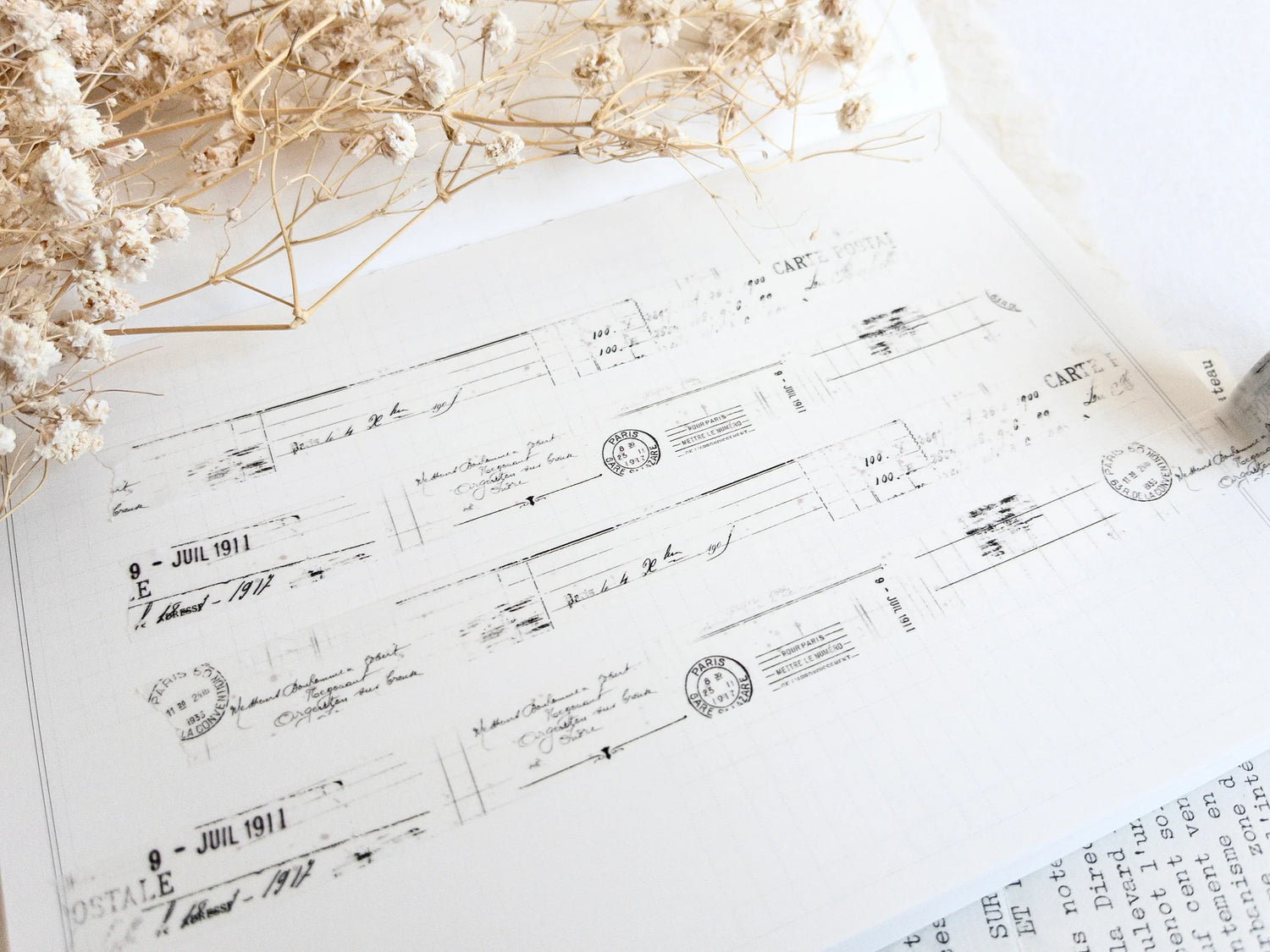 Washi tape with distressed vintage elements on light background with dried flowers next to it