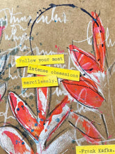 A close-up of a textured kraft paper print featuring abstract red and orange floral brushstrokes, white script writing, small blue paint splatters, and yellow paper tabs with text including &