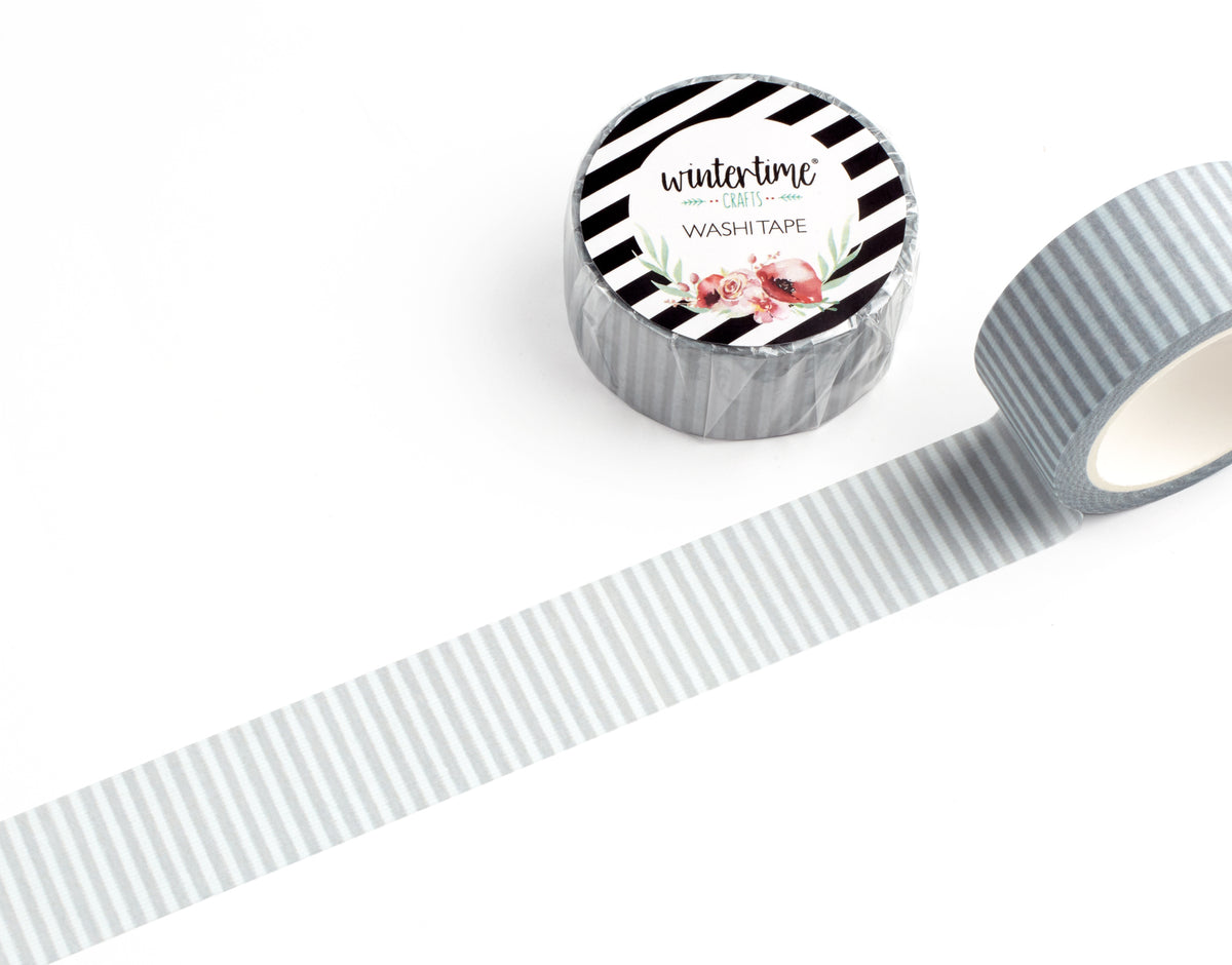 A roll of washi tape with a gray and white striped pattern, shown partially unrolled on a clean white background. The top of the roll features a circular label with black and white diagonal stripes, the brand name &