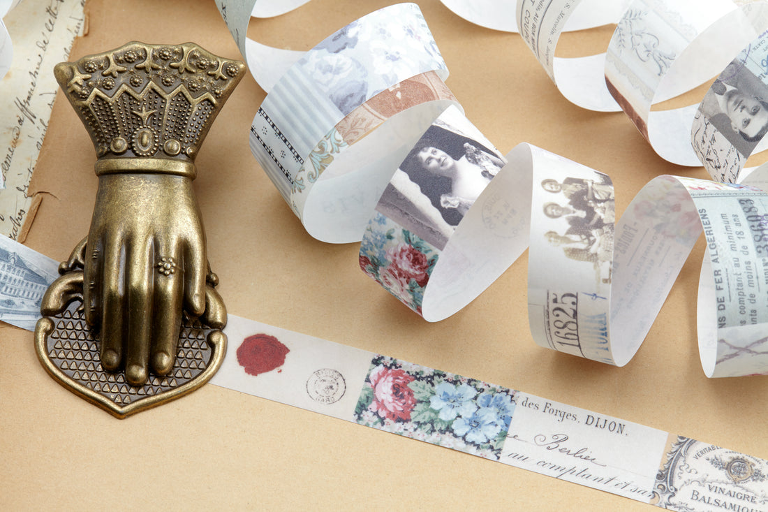 A decorative antique bronze hand-shaped clip displayed on a beige surface with rolled vintage paper washi tape next to it.