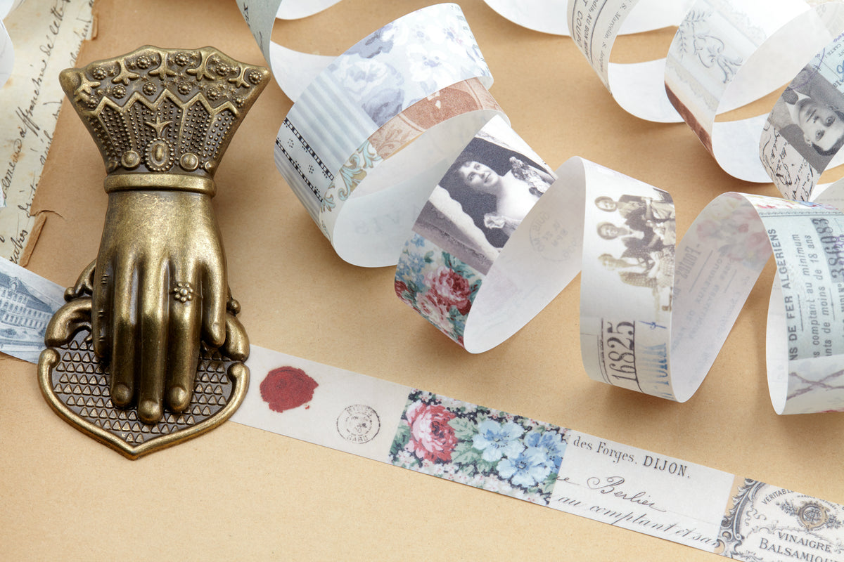 A decorative antique bronze hand-shaped clip displayed on a beige surface with rolled vintage paper washi tape next to it.