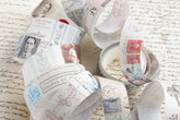 A collection of decorative washi tape printed with vintage postage stamps, postmarks, and classic portraits, arranged on top of a background of handwritten paper.