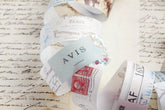 A close-up of decorative washi paper roll featuring vintage-style printed designs, including a light blue card reading &