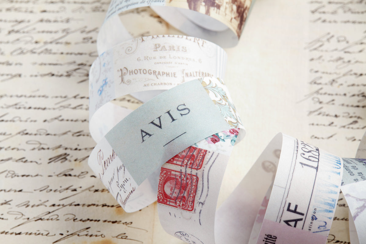A close-up of decorative washi paper roll featuring vintage-style printed designs, including a light blue card reading &