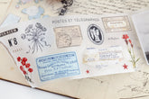 PET tape with pre-cut vintage-style decorative stickers such as illustrated labels, postage stamps, numbers, and antique typography, laid over a background of old handwritten letters and papers.