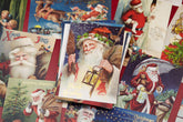 A pile of vintage Christmas greeting cards featuring illustrations of Santa Claus in red and white, with one central card showing Santa holding a lantern and the words &