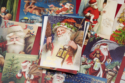 A pile of vintage Christmas greeting cards featuring illustrations of Santa Claus in red and white, with one central card showing Santa holding a lantern and the words &