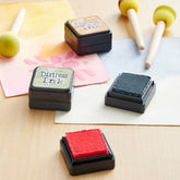 Four Distress Ink stamp pads in different colors arranged on a light wood table with craft tools like foam tools and paper.