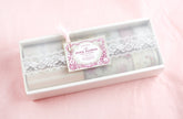 A boxed set of floral lace items in a white rectangular package with a clear lid, decorated with white lace and a pink floral tag reading &
