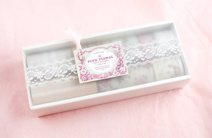 A boxed set of floral lace items in a white rectangular package with a clear lid, decorated with white lace and a pink floral tag reading &