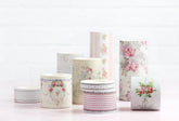 A collection of decorative paper washi tapes with floral and striped patterns, arranged on a light pink surface against a white brick wall background.