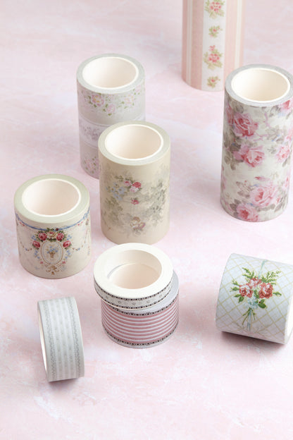 A set of decorative washi tapes in soft pastel colors, featuring floral, striped, and patterned designs, arranged on a light pink background.