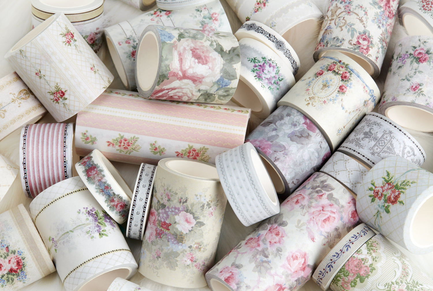 A pile of decorative washi tapes with vintage floral and patterned designs in soft pastel colors, including pink, green, gray, and cream.