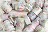 A pile of decorative washi tapes with vintage floral and patterned designs in soft pastel colors, including pink, green, gray, and cream.