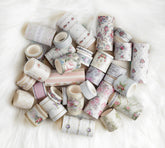 A pile of decorative washi tapes with various floral, geometric, and striped patterns in soft pastel colors, arranged on a white faux fur surface.
