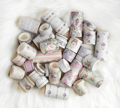 A pile of decorative washi tapes with various floral, geometric, and striped patterns in soft pastel colors, arranged on a white faux fur surface.